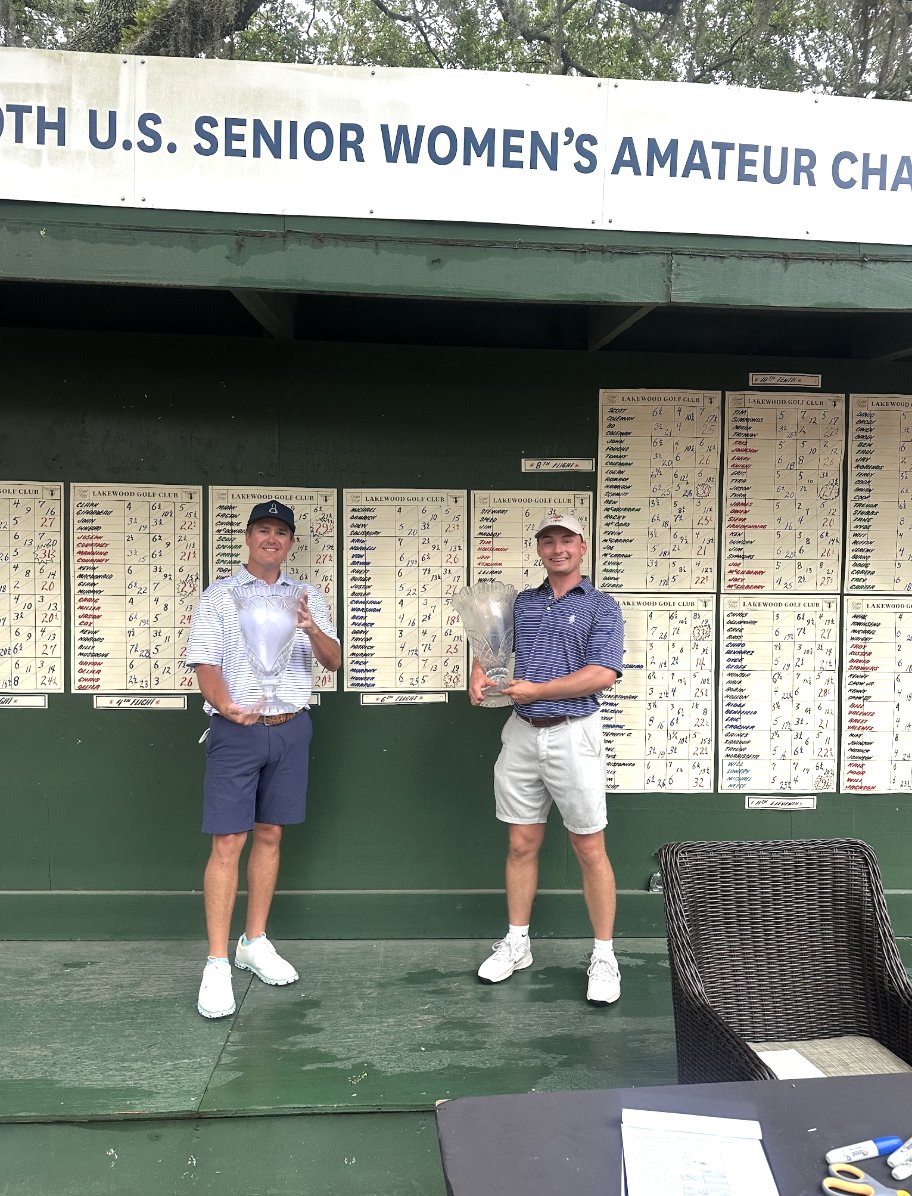 Zach Murphy and Hunter Harper holding their crystal trophies in front of the tournament scoreboards