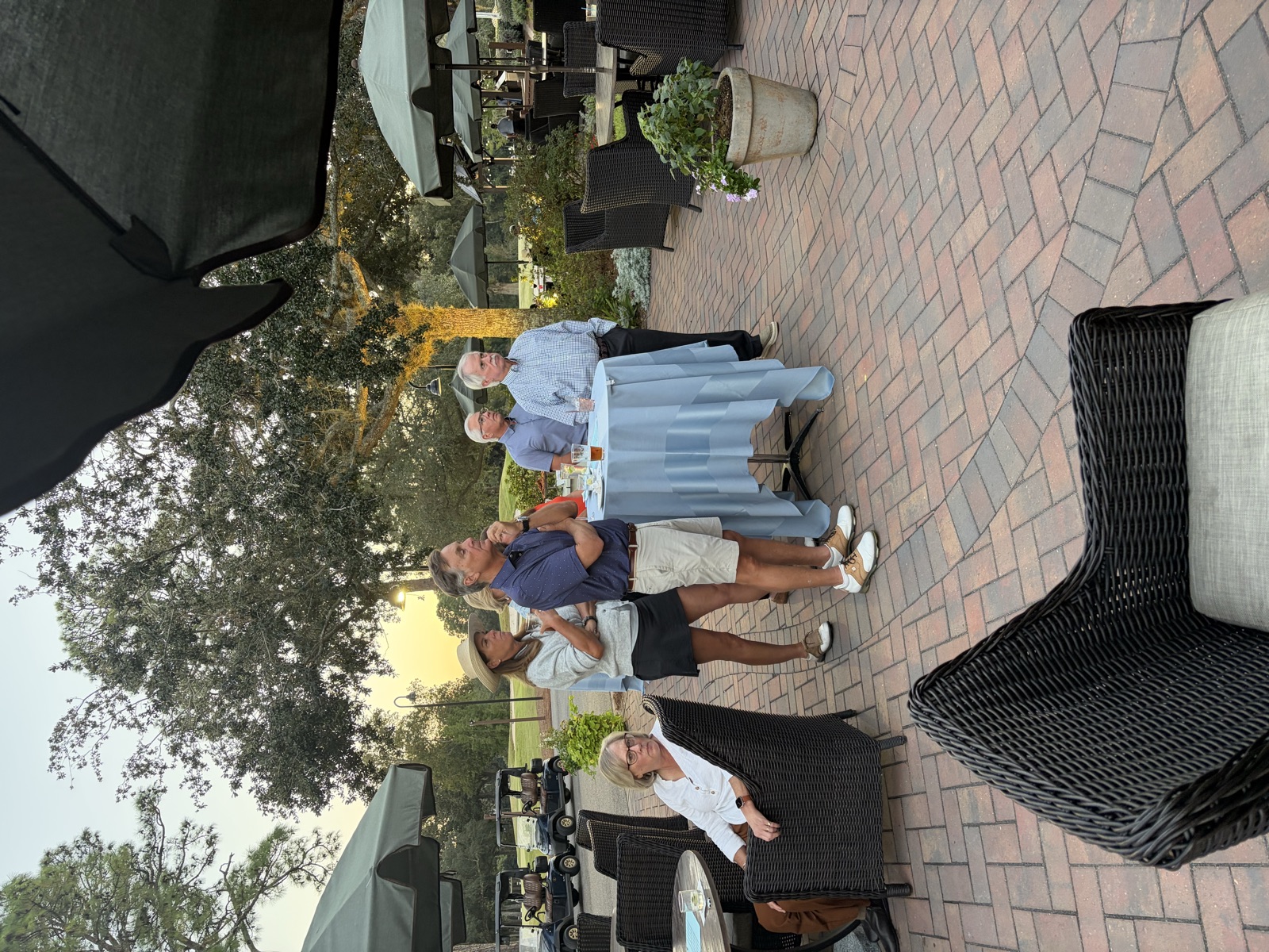 Members standing and listening on the patio as the sun sets behind the trees