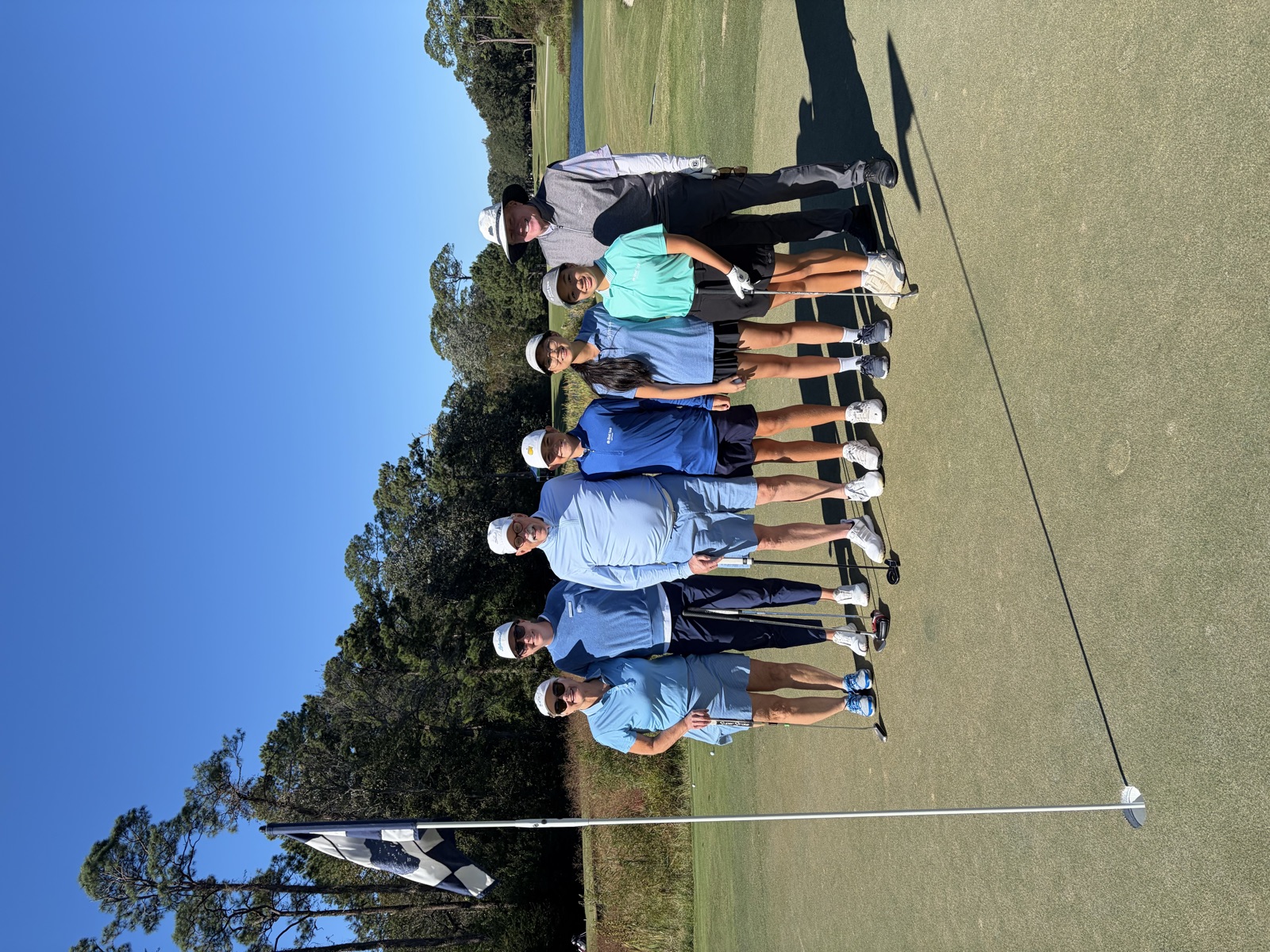 A group of players and junior golfers standing on the green beside the flagstick