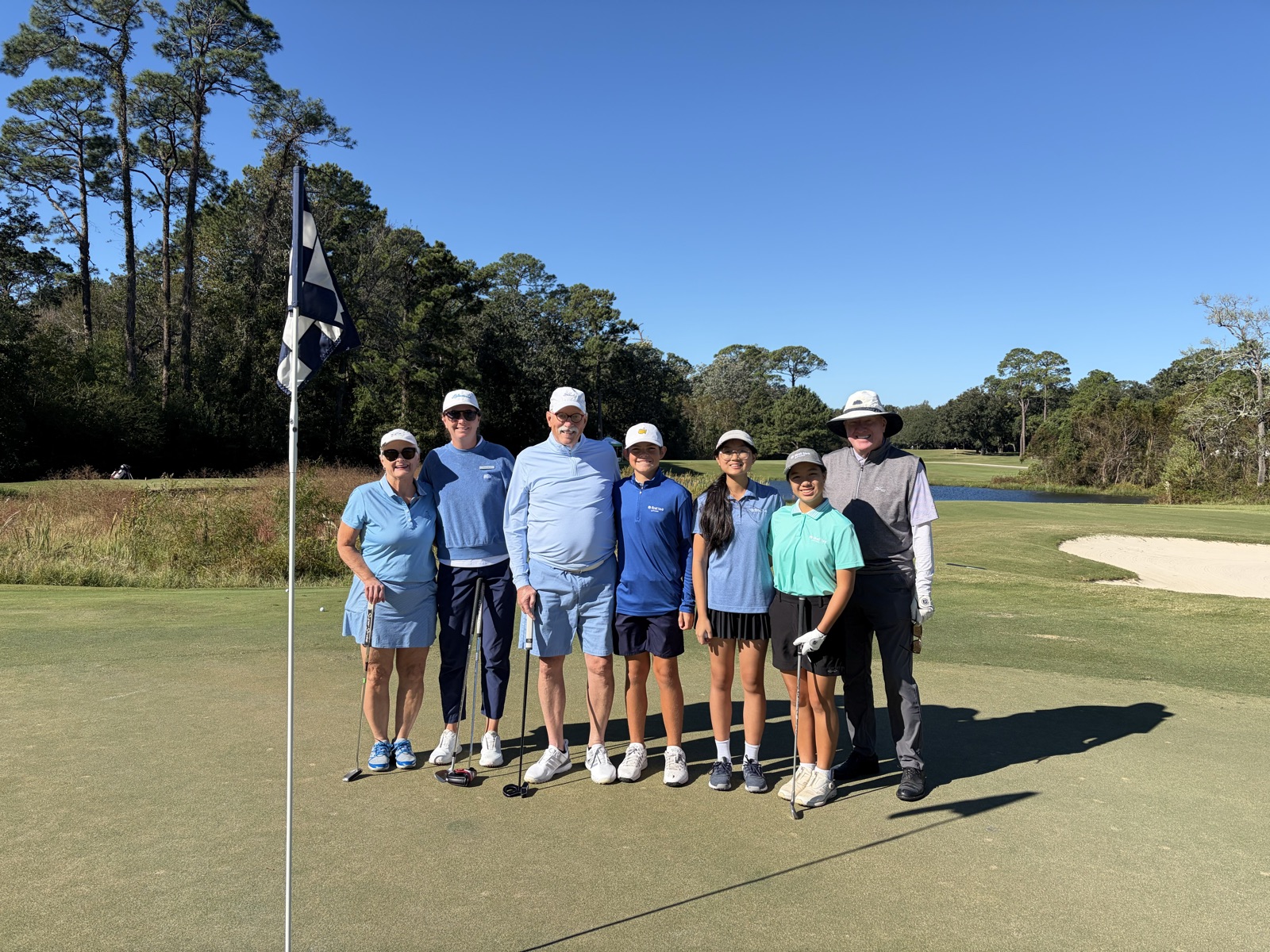 Players and junior golfers lined up on the green on a clear morning